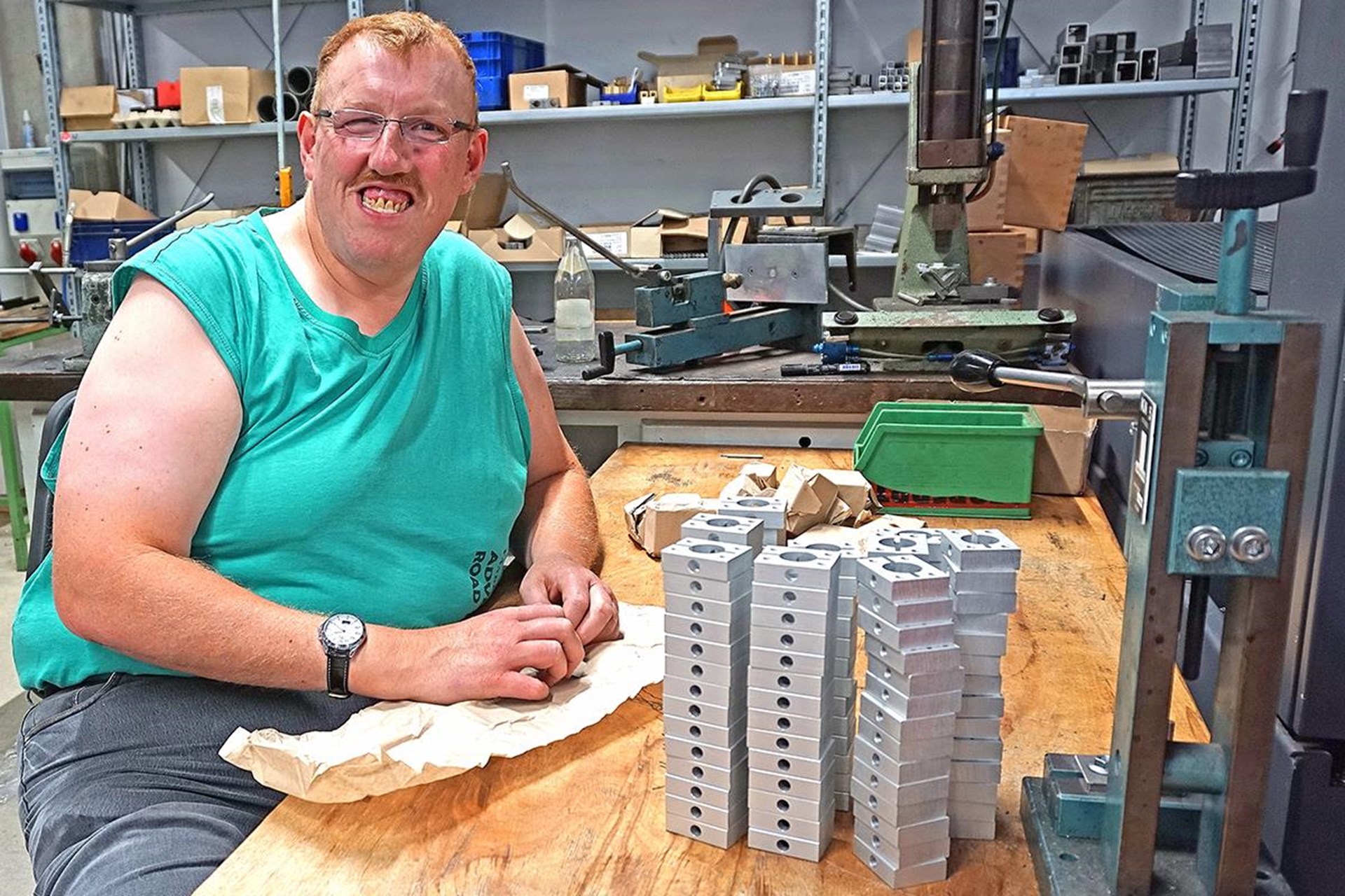 Mitarbeiter sitzt an einem Arbeitstisch in der Metallwerkstatt und sortiert gestapelte Metallteile.