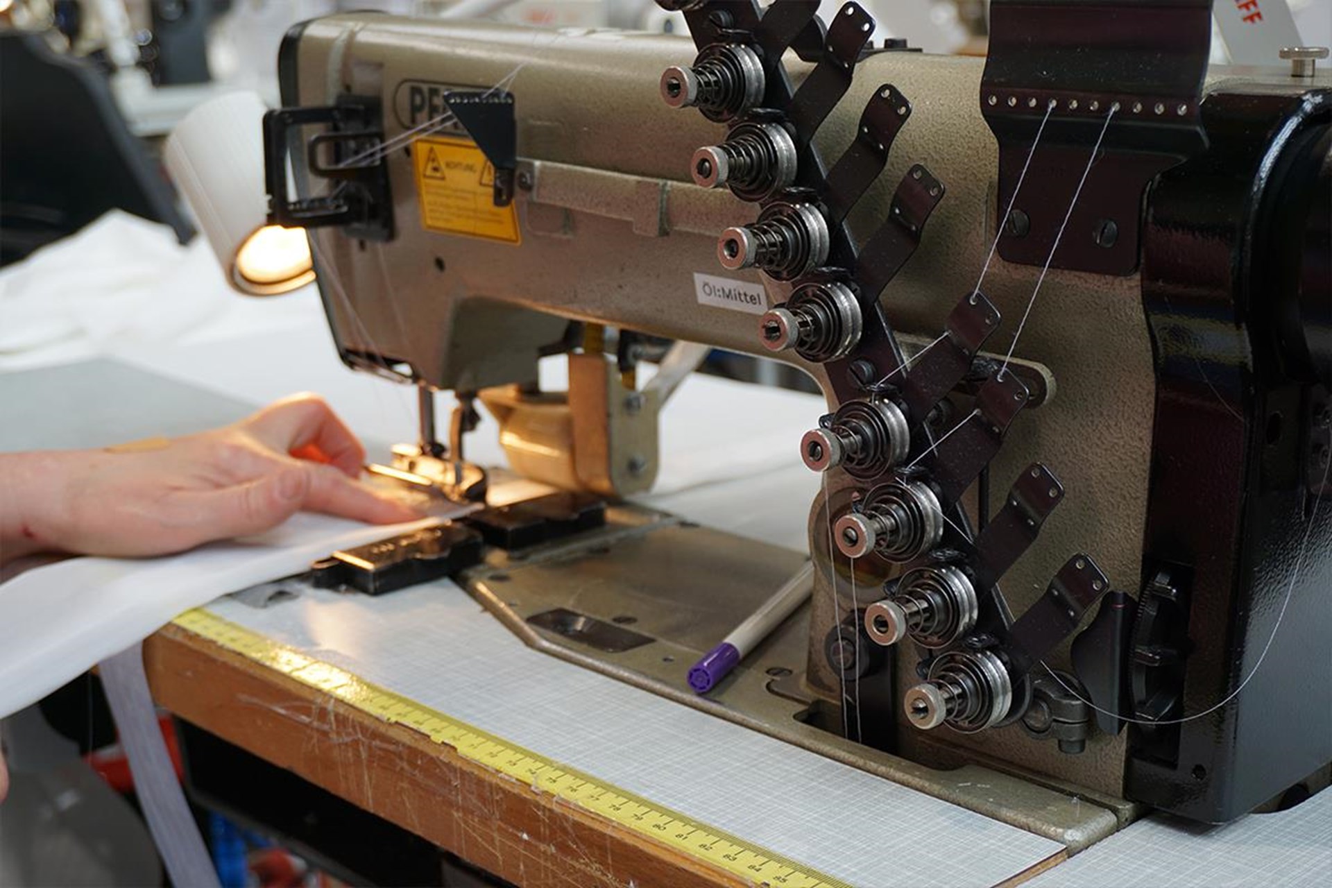 Hand führt Stoff unter einer Industriemaschine beim Nähen in der Näherei der Wolfsteiner Werkstätten.